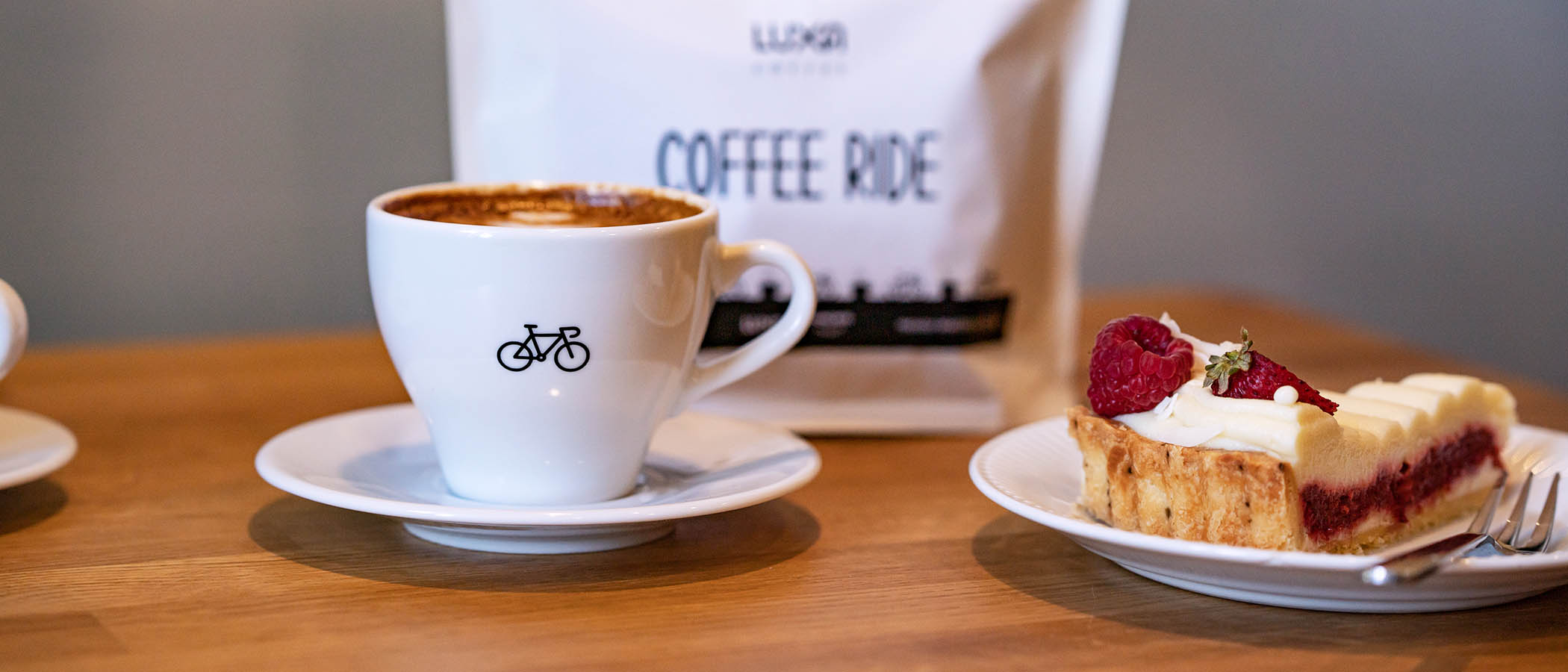 st&oacute;ł w kawiarni z filiżanka Luxa z rowerem, ciastko i w tle kawa dla kolarzy Luxa